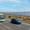 Electric bus and electric car with green number plates on an Indian expressway lined with solar panels and wind turbines